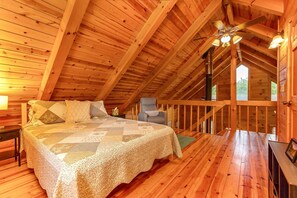 A wooden cabin bedroom with a bed, a chair, a ceiling fan, and a view of the outdoors.