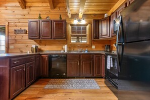 A kitchen with wooden cabinets, a dishwasher, a refrigerator, and a window above the sink.