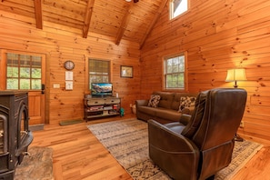 Ein gemütliches Blockhaus-Interieur mit Kamin, einer Couch, einem Fernseher und Holzwänden.