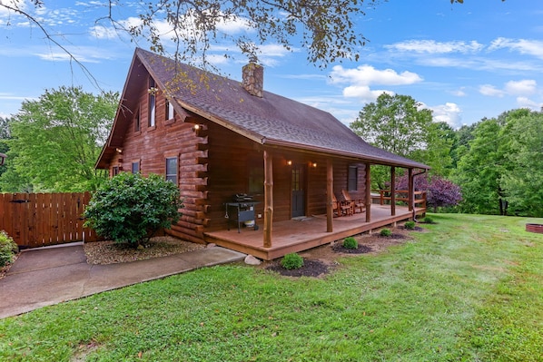 A log cabin with a porch, a grill outside, and a wooden deck.