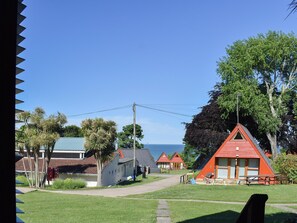 Une zone côtière avec plusieurs cabanes aux toits rouges, un sentier bordé d’herbe et une vue sur la mer.