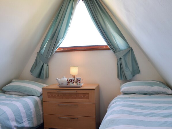 Une chambre avec deux lits, une table de chevet avec une lampe et une fenêtre avec des rideaux.