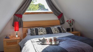 A bedroom with a sloped ceiling, a bed with patterned pillows, a bedside table with a lamp, and a tray with teapot and cups. - 2 bedroom accommodation in Kingsdown, near Deal (Kingsdown, near Deal)