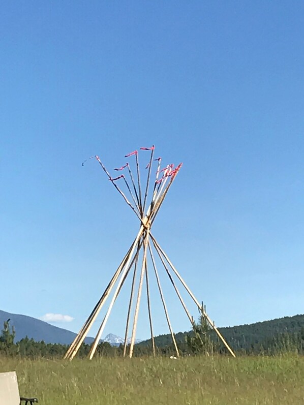 A large, open field with a tall, slender structure made of metal poles and red flags, set against a clear blue sky and a mountain in the background.