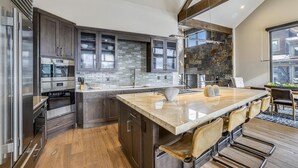 A modern kitchen with dark cabinets, a large island, and a stone backsplash.