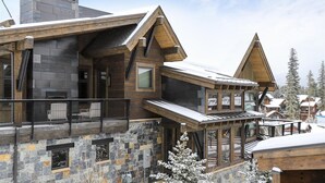 A modern lodge with a stone facade, wooden balconies, and a ski slope view.