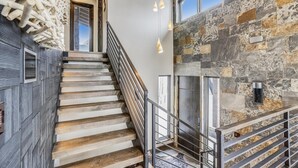 A staircase with wooden steps and a metal railing, leading to a stone wall with a fireplace.
