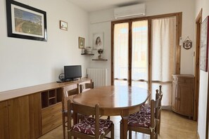 A dining area with a round table, chairs, a TV, and a window with curtains.