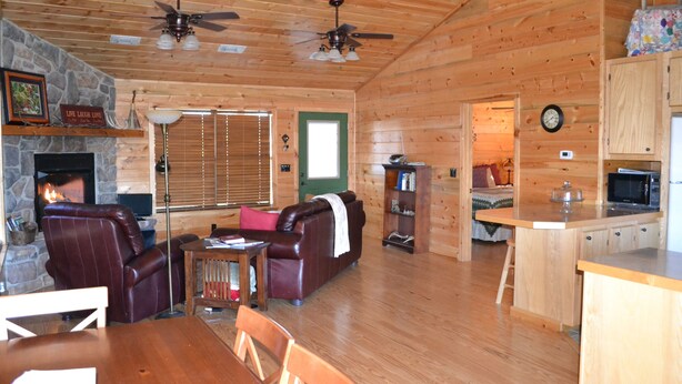 L’intérieur chaleureux d’un chalet avec une cheminée en pierre, des fauteuils en cuir, un plancher en bois et un coin cuisine.