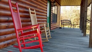 Une cabane en bois dotée d’un porche comprenant deux fauteuils à bascule et un banc.