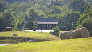 Un paysage rural avec un bâtiment rouge, des bottes de foin et un étang.