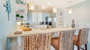 A modern kitchen with a central island, bar stools, and pendant lighting. - Wake up to the rhythm of the Atlantic. (St. Simons Island)