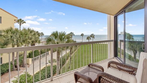 A balcony with wicker furniture, a view of the beach, and palm trees. - Wake up to the rhythm of the Atlantic. (St. Simons Island)