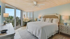 A bedroom with a large bed, a ceiling fan, a nightstand, and a view through a sliding glass door. - Wake up to the rhythm of the Atlantic. (St. Simons Island)