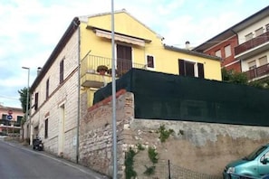 Un bâtiment jaune avec un balcon, un mur en briques et une voiture garée.