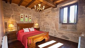 A bedroom with a stone wall, wooden bed, two bedside lamps, a chandelier, and a window. - Full rental house for 8-10 people, ideal for families with pets. (Ponte-Caldelas)