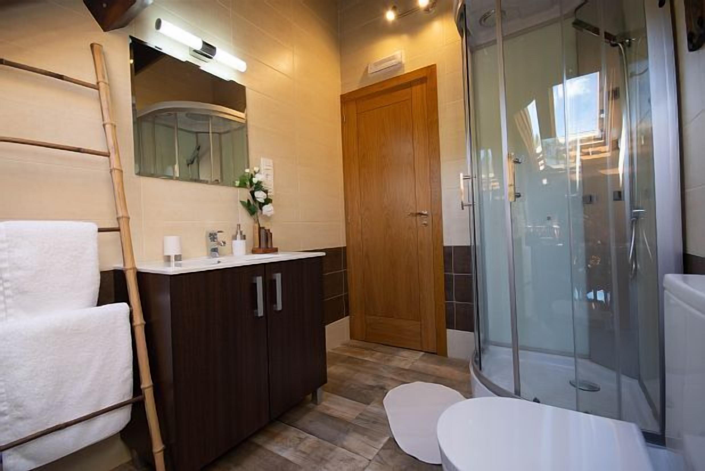 Un bagno con un mobile vanitario in legno, un box doccia in vetro e un water bianco.