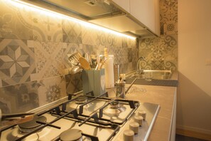 Kitchen features a gas stove, sink, and knife block, with decorative tiles and a countertop.