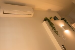Quarto com ar condicionado branco, uma pequena planta e luminária fixada na parede.
