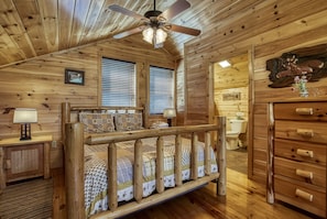 Cozy cabin-style bedroom with a wooden bed, dresser, and nightstand, featuring a ceiling fan and window with blinds.
