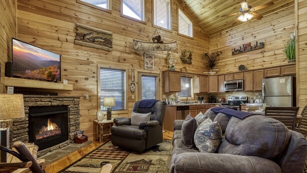 A cozy log cabin interior with a fireplace, leather recliner, and a dining area.