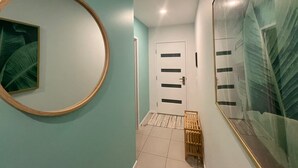A hallway with a circular mirror, a door with horizontal slats, and a large framed picture on the wall.