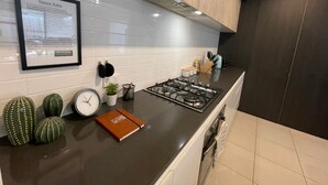 A modern kitchen with white tiled walls, a gas stove, a clock, and a framed document on the wall.