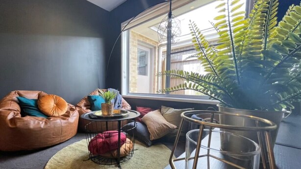 A cozy room with a large window, a bean bag chair, a small round table, and a potted plant.