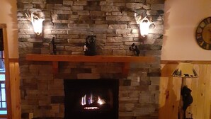 Una sala de estar con chimenea de piedra, un ventilador de techo y un reloj en la pared.
