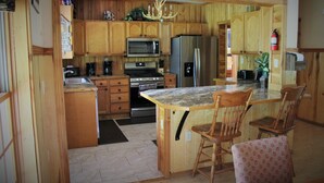 Una cocina con armarios de madera, microondas, refrigerador y una barra con dos sillas de madera.