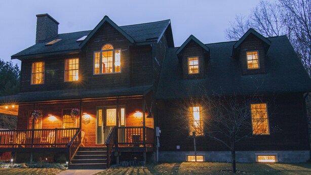 Una casa grande de madera con varias ventanas y un porche, con luces colgantes y una escalera que lleva a la entrada.