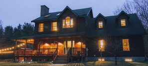 A large wooden house with multiple windows and a porch, featuring string lights and a staircase leading to the entrance. - SLEEPS 16, 7 bedroom 4 baths w/ 2 game rooms, SXS rentals w/direct trail access (Atlanta)