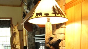Una lámpara de madera con forma de oso y una silueta de oso en la pantalla, una chimenea de piedra y una decoración con cabeza de venado.