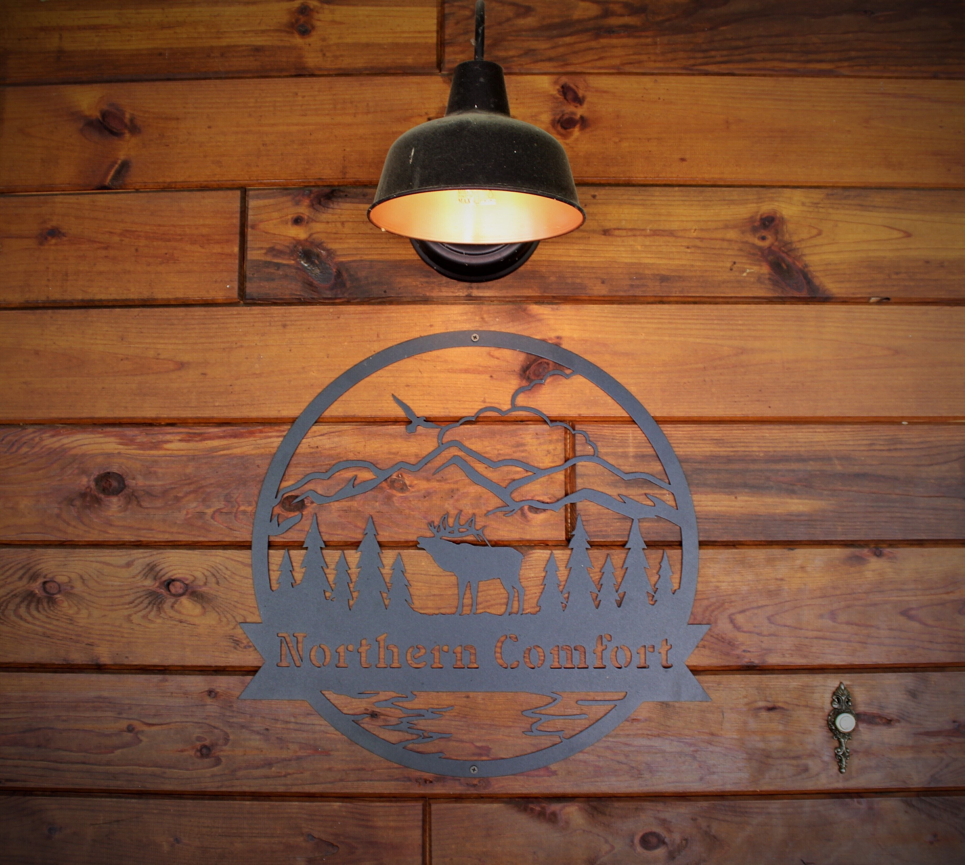 Un mur en bois orné d’un logo circulaire représentant un élan et des arbres, avec une lampe suspendue au-dessus.