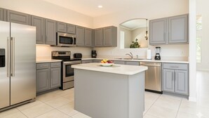 Una cocina moderna con gabinetes grises, electrodomésticos de acero inoxidable y una isla central con fruta.