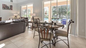 Un salón espacioso con un sofá gris, una mesa de comedor con sillas y un amplio ventanal con vistas a una piscina.