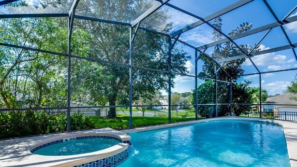 Una piscina techada con un jacuzzi, rodeada de vegetación exuberante y un cielo azul despejado.