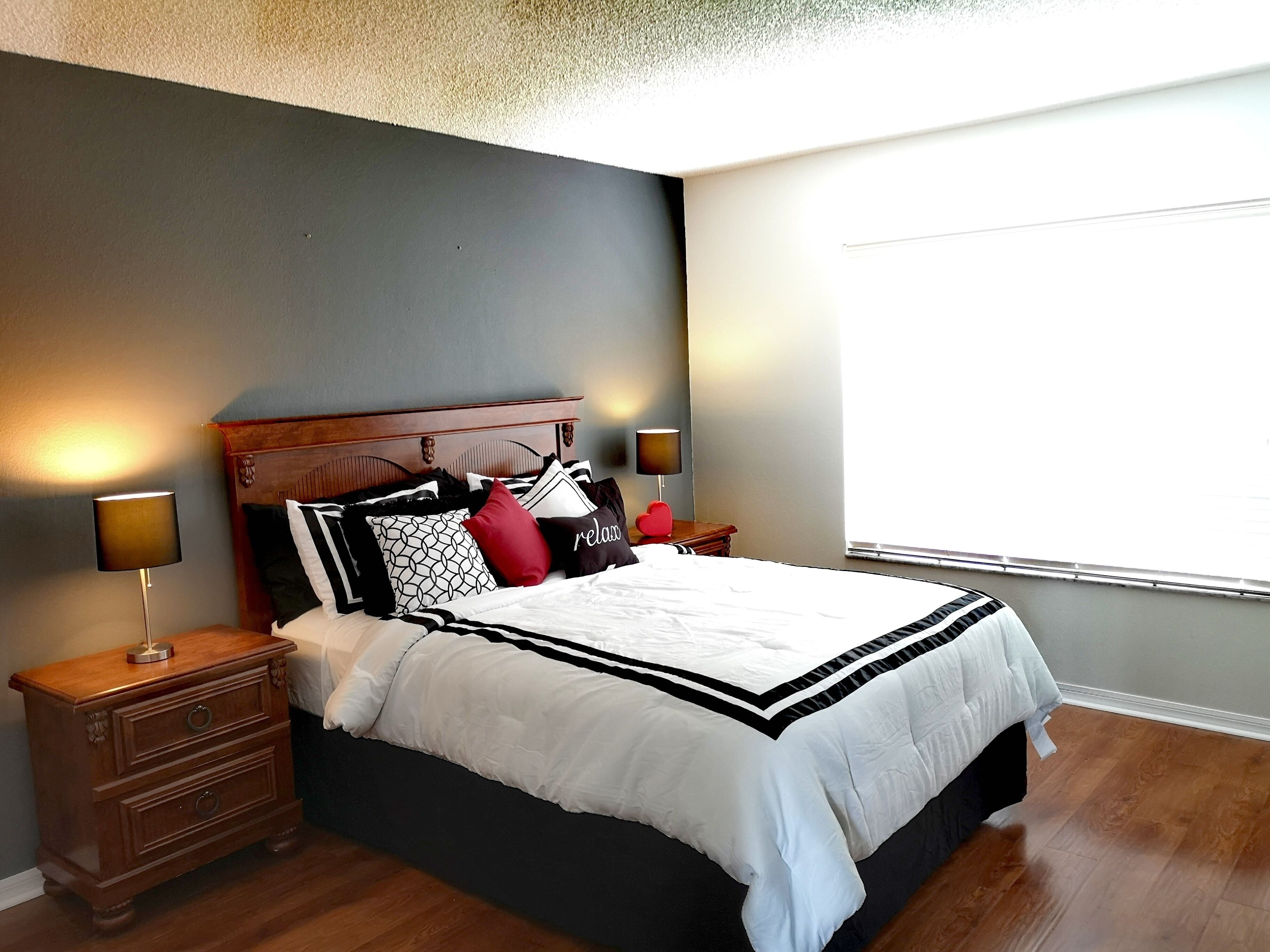 Een net opgemaakt bed met een zwart-wit dekbed, met aan weerszijden nachtkastjes met lampen, in een kamer met houten vloeren en een grijze accentmuur.