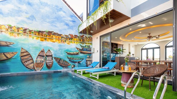 A swimming pool with lounge chairs, a mural of boats, and a restaurant area with tables and chairs. - Seaweed Luxury Villa&Spa (Da Nang)