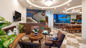A hotel lobby with a reception desk, seating area, staircase, and a large window with a view of the city. - Seaweed Luxury Villa&Spa (Da Nang)