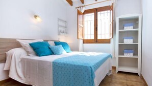 A bedroom with a bed, a window with curtains, a shelf with storage boxes, and a wall-mounted light.