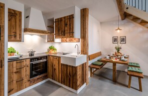 A modern kitchen with wooden cabinetry, a built-in oven, and a dining area with a bench and table. - Granary 88sqm, 2 bedrooms, 2 bathrooms, fireplace, sauna, gallery (Eggstätt)