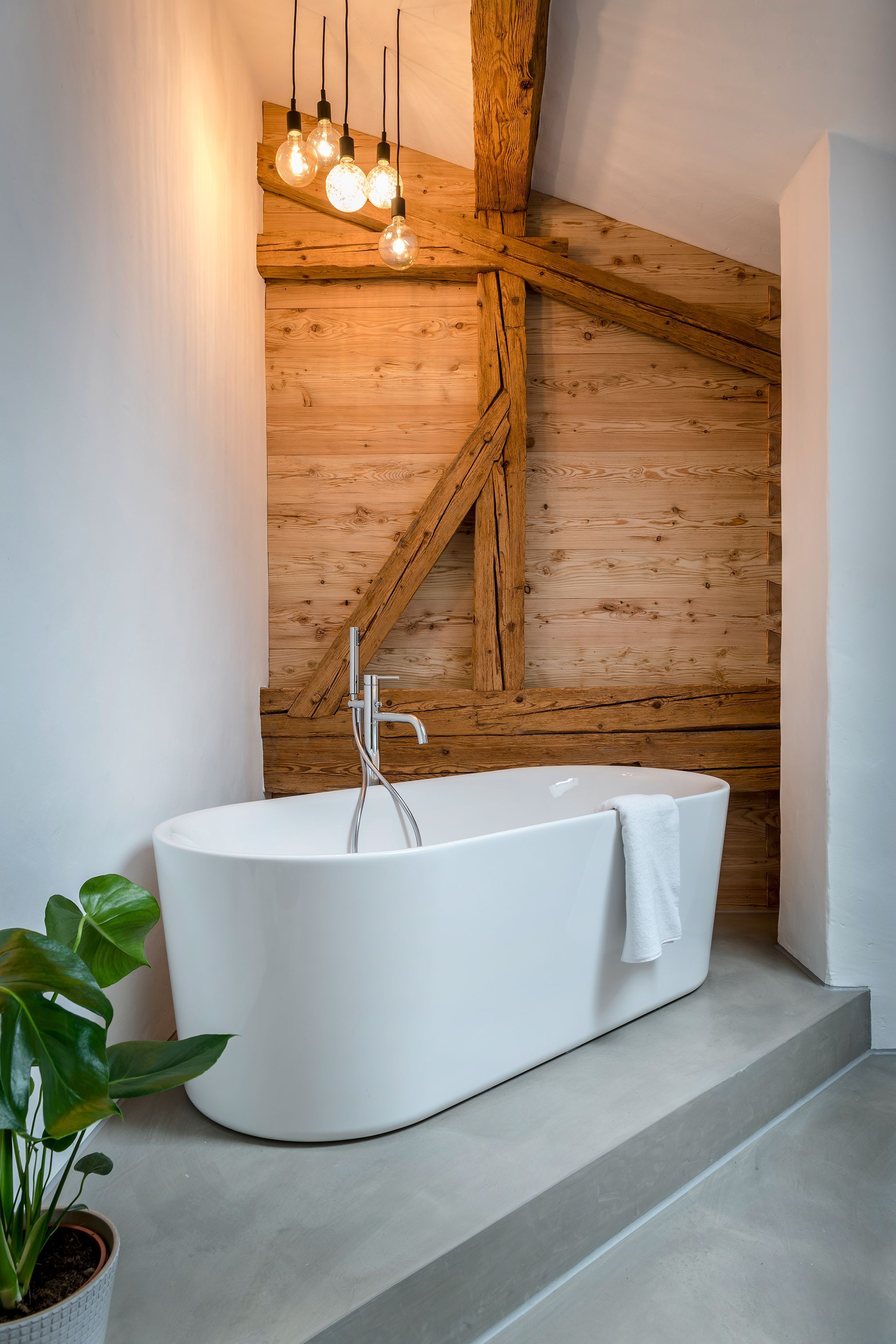 Une salle de bain moderne avec une baignoire sur pieds, des poutres en bois et des luminaires suspendus.