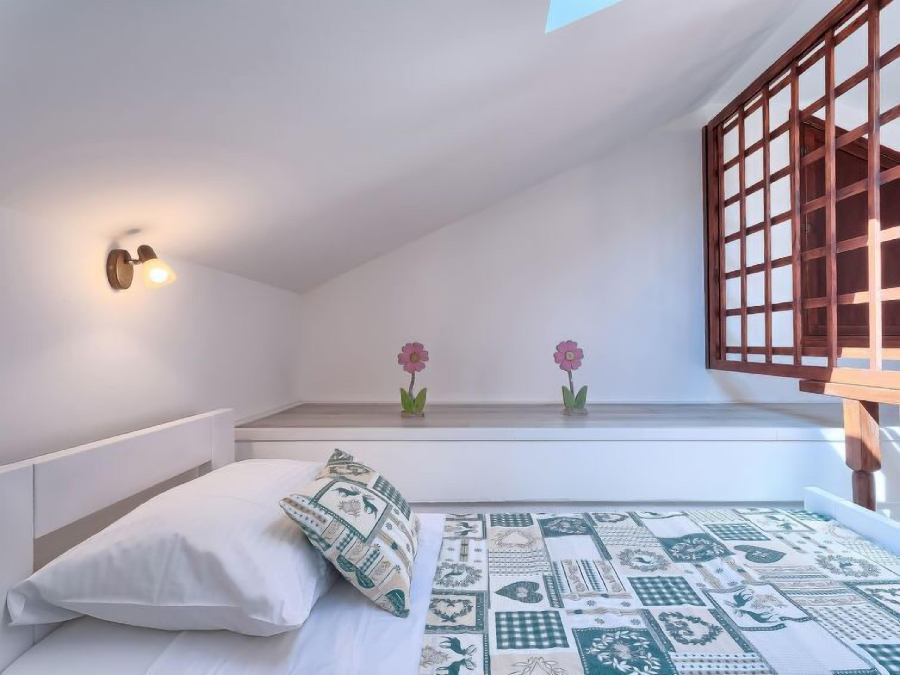 A bedroom with a bed, pillows, a patterned rug, a wooden bench, and two wall-mounted lights.