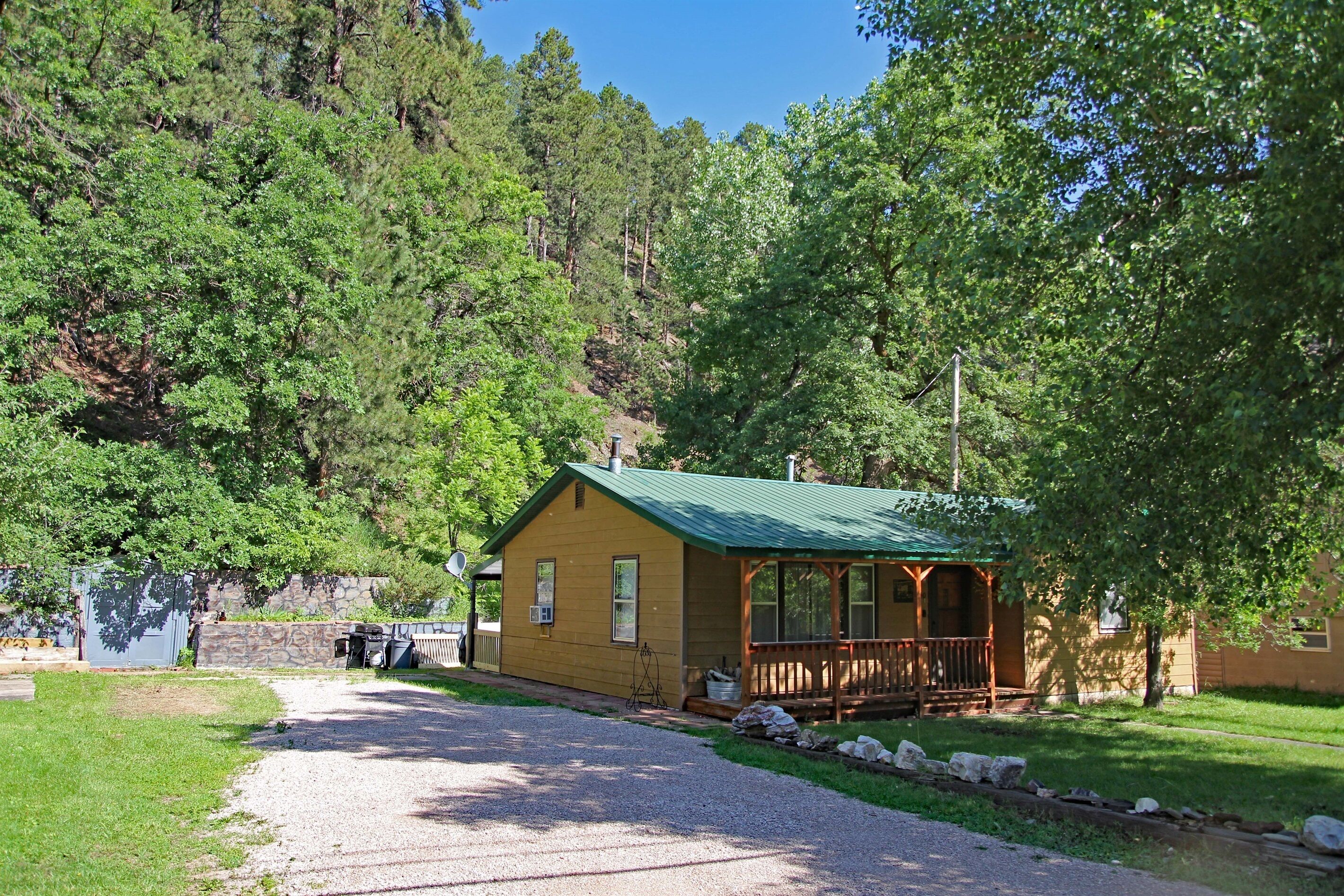 Une cabane dotée d’un toit végétalisé, entourée d’arbres, et accessible par une allée en gravier.