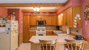 A compact kitchen with wooden cabinets, a refrigerator, microwave, stove, and a small dining area with two chairs.