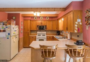 Kitchen features a central island with two chairs, refrigerator, microwave, stove, and sink.