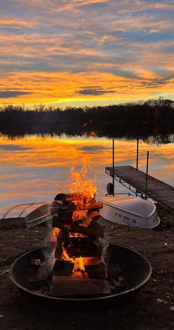 A campfire with a boat and dock in the background.