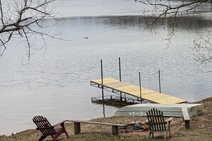 A wooden dock extending into a calm lake, with two Adirondack chairs on the shore.