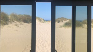 Blick durch ein Fenster auf einen Sandstrand und Dünen im Hintergrund.